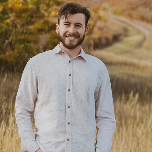 Man smiling in a field with trees.