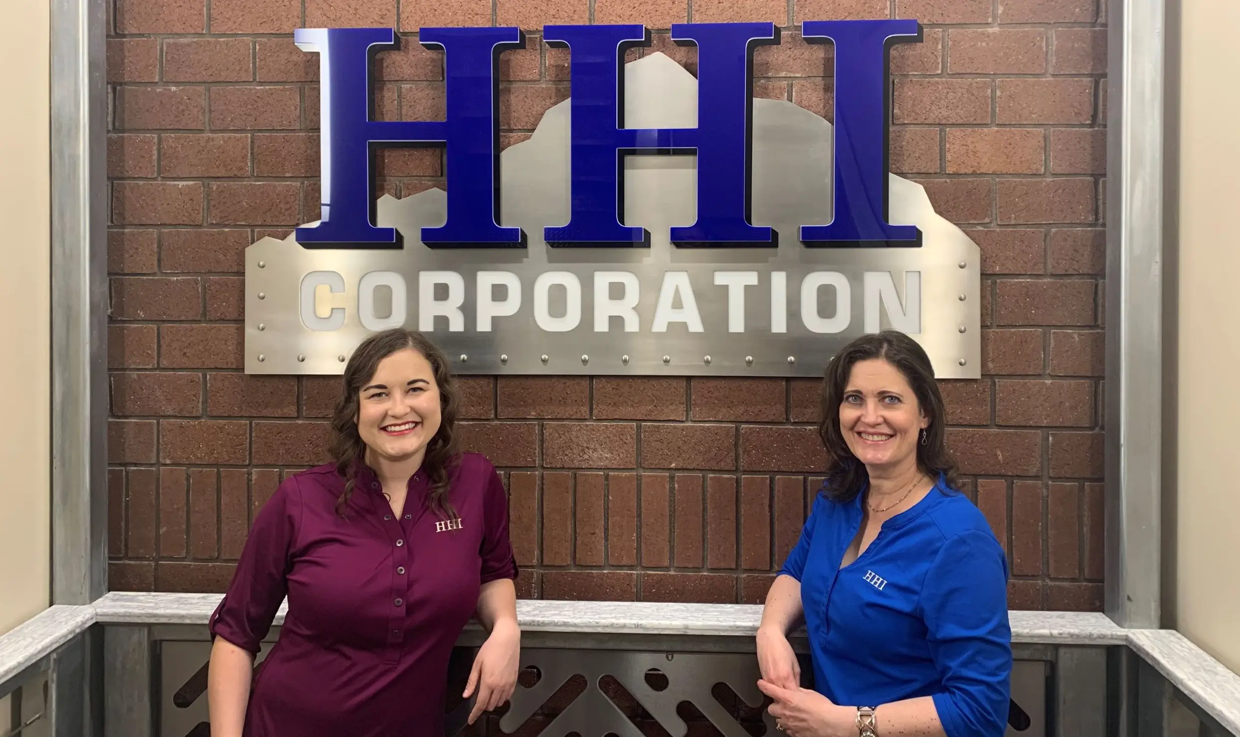 Women posing by HHI Corporation sign.