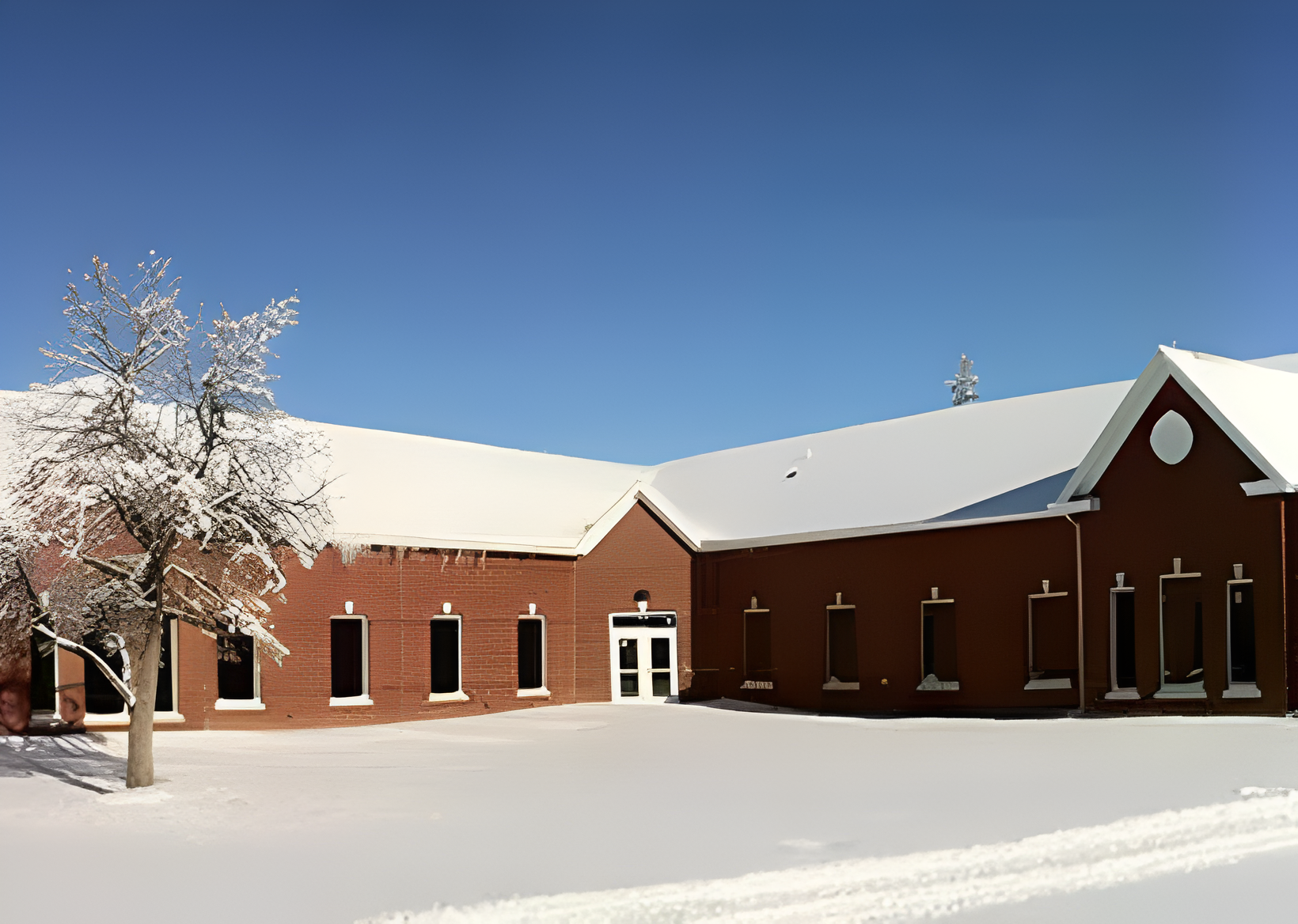 Snow-covered red brick building and tree.
