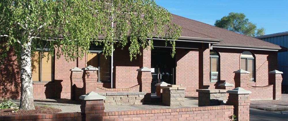 A brick house with a covered porch and a tree in the yard.