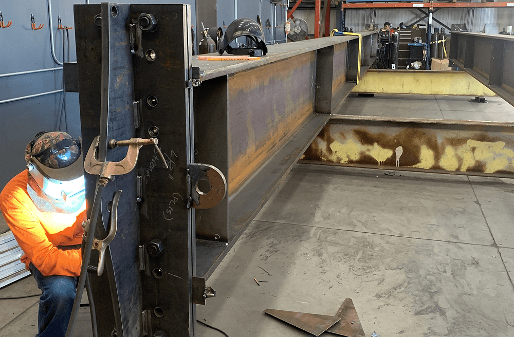 Welder working on large metal beam indoors.